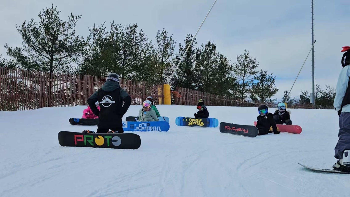 An instructor teaching a group of young snowboarders sitting on the snow
